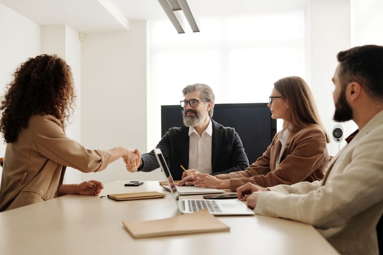 Four business professionals meeting around a table as two shake hands